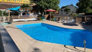 A swimming pool with a wooden deck, lounge chairs, and a shaded area with umbrellas. - ZEcamping 3 étoiles piscine chiens acceptés locatif TV 28m2 6 pers (La Tremblade)