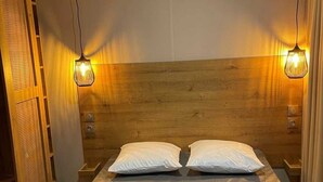 A bedroom with a wooden headboard, two bedside tables, a bed with grey bedding, and two pendant lights. - ZEcamping 3 étoiles piscine chiens acceptés locatif TV 28m2 6 pers (La Tremblade)
