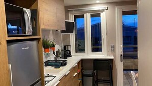 A compact kitchen with wooden cabinets, a built-in refrigerator, a small island with a sink, and a window providing natural light. - ZEcamping 3 étoiles piscine chiens acceptés locatif TV 28m2 6 pers (La Tremblade)