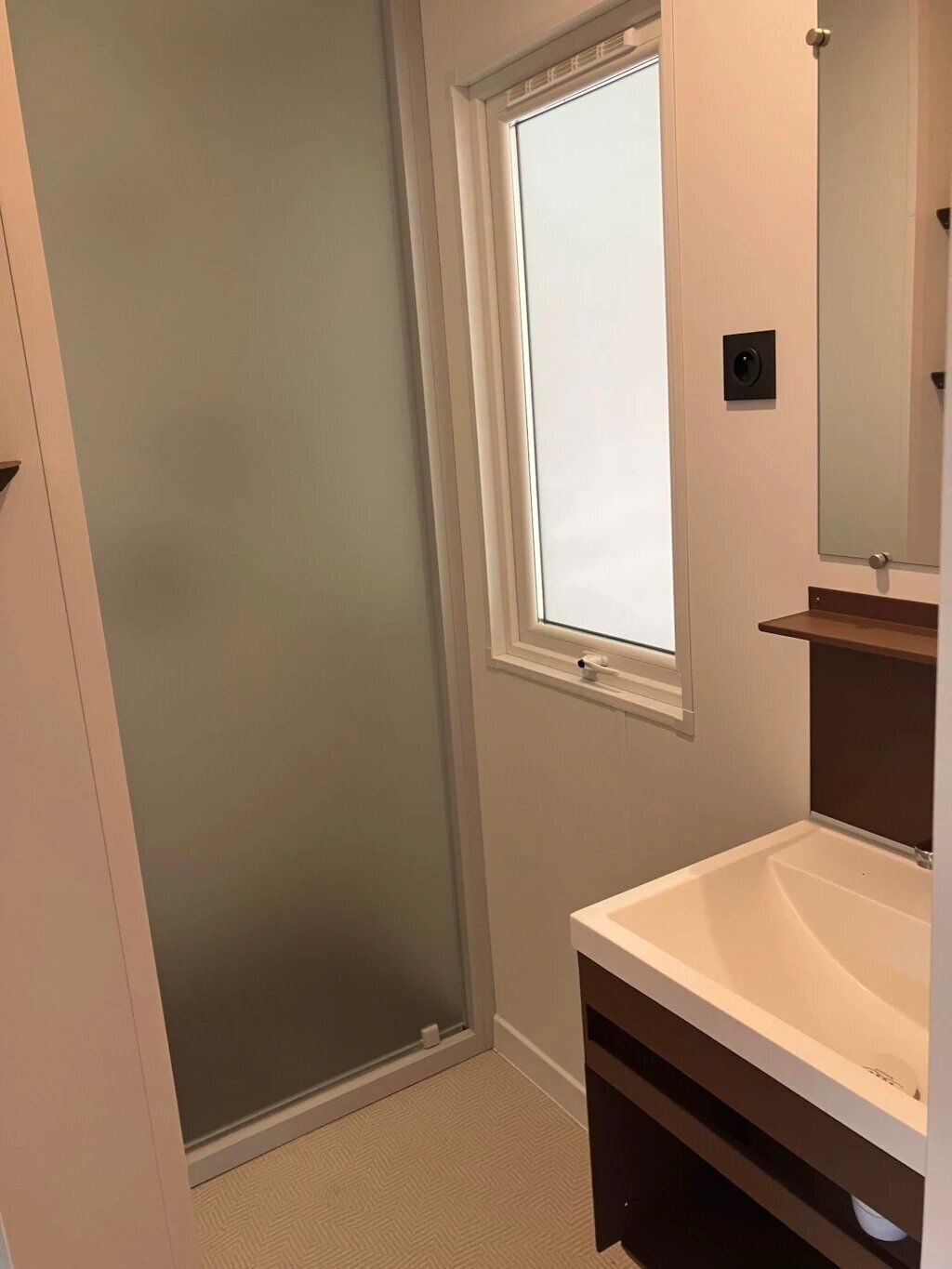 Un baño con ducha, ventana, lavamanos y espejo.