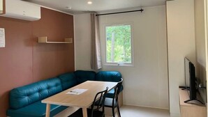 A compact room with a teal sofa, a small wooden table, and a TV on a wooden stand.