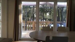 Quarto com uma grande porta de vidro deslizante que dá para uma varanda com guarda-corpo de madeira. No interior, há uma mesa redonda com cadeiras.