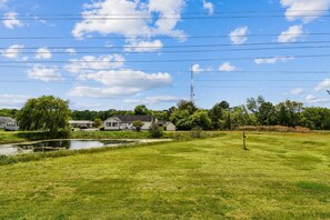 Ein grünes Feld mit einem Teich, Häusern und einer Stromleitung im Hintergrund.