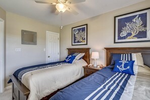 Ein Schlafzimmer mit zwei Betten, einem Deckenventilator, einem Nachttisch mit Lampe und gerahmten Kunstwerken an den Wänden.