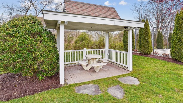 A covered patio area with a table and benches, surrounded by a white fence and greenery. - Townhome with community pool, tennis court, and only 2 miles from Bethany Beach! (Frankford)