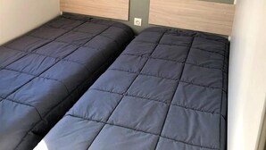 Una habitación con dos camas individuales, cada una con cabecero de madera y una pared gris detrás.