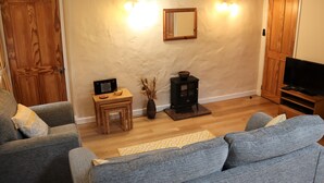 Una sala de estar con dos sofás grises, una mesa de centro de madera, una pequeña mesita auxiliar de madera, un mueble para televisor y una chimenea.