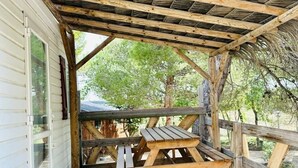 En træterrasse med et picnicbord og et overdækket område med stråtæppe.