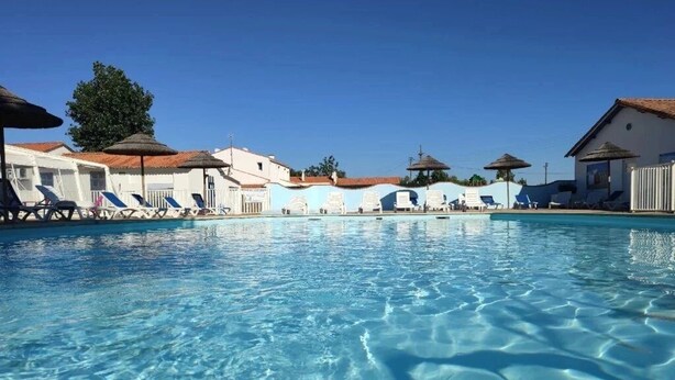 Une piscine aux eaux cristallines, agrémentée de chaises longues et de parasols, et entourée d’immeubles présentant un style architectural uniforme.
