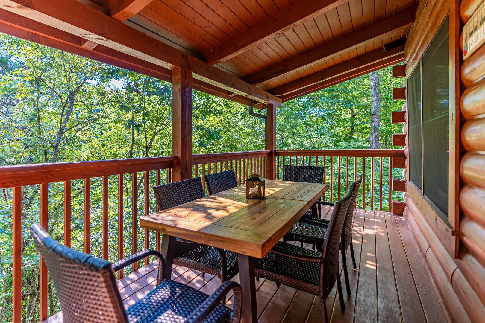 Une terrasse en bois, agrémentée d’une table et de chaises, entourée d’une rambarde et offrant une vue sur une zone boisée.