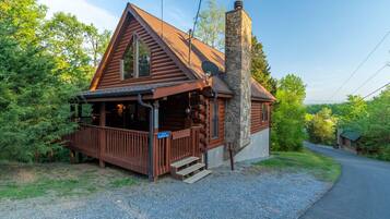 Step up to the charming cabin with a wooden porch and stone chimney, surrounded by lush greenery.