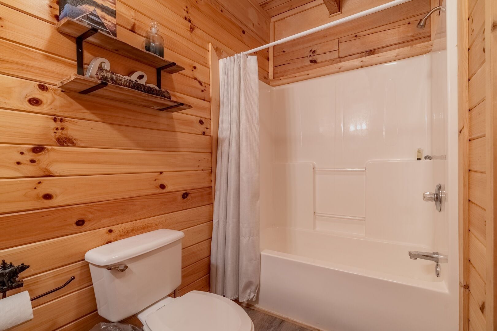 A wooden-paneled bathroom with a toilet, a shower with a curtain, and a shelf with toiletries.