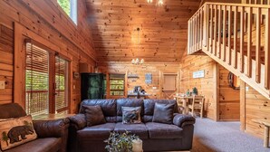 Interior de una cabaña de madera con sofá de cuero, una mesa de comedor y una escalera.