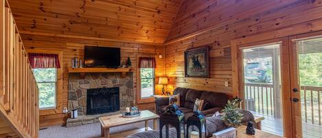 A cozy cabin interior with a stone fireplace, wooden walls, a television, and a 'be our guest' sign.