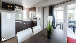 A modern kitchen with a refrigerator, stove, microwave, and cabinets. There is a dining table with chairs and a potted plant.