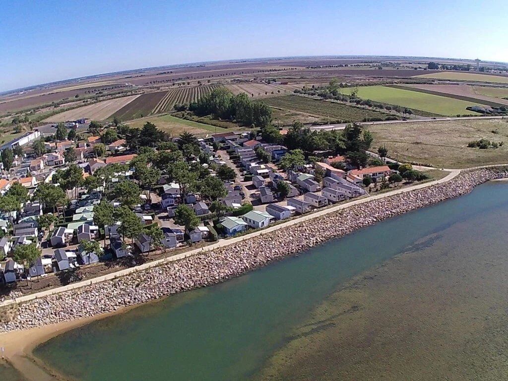 Luchtbeeld van een kustdorp met huizen langs een rotsachtige kustlijn en velden op de achtergrond.