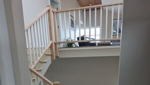 Eine Treppe führt zu einer zweiten Etage mit Holzbalkendecke und Blick auf die darüberliegende Ebene.