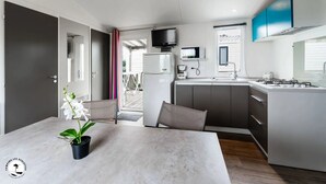 Een compacte keuken met een eethoek, een televisie boven het fornuis en uitzicht op het terras.