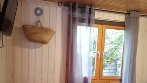 Una habitación con paredes de madera, una cama, una silla, un televisor y una ventana con cortinas.