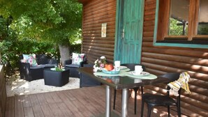 Una cabaña de madera con terraza, amueblada con asientos exteriores y una mesa dispuesta para dos.