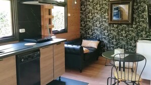 Una cocina funcional con lavavajillas, estufa negra y un mueble de madera. Se aprecia un sofá negro y una pequeña mesa redonda con sillas.
