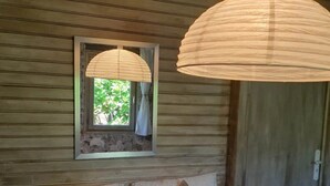Habitación de cabaña de madera con una cama, dos lámparas colgantes, una ventana con vistas a follaje y una puerta.