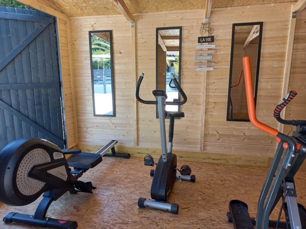 Une salle de sport équipée de matériel d’exercice, avec des murs en bois et un mur recouvert de miroirs.