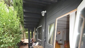Un espacio al aire libre techado con una mesa, sillas, un banco y una puerta que da a un área interior.