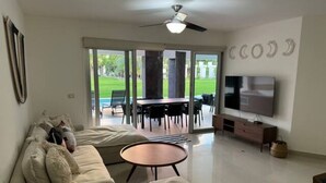 A modern living room with a sofa, a coffee table, a TV, and a balcony with outdoor furniture. - Amazing Apt for 10, big beach, private pool jacuzzi & BBQ, fully equipped (Playa del Carmen)