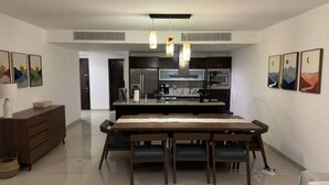 A modern kitchen with dark cabinets, a stainless steel refrigerator, and a built-in oven. There is a dining table with chairs in the center of the room. - Amazing Apt for 10, big beach, private pool jacuzzi & BBQ, fully equipped (Playa del Carmen)