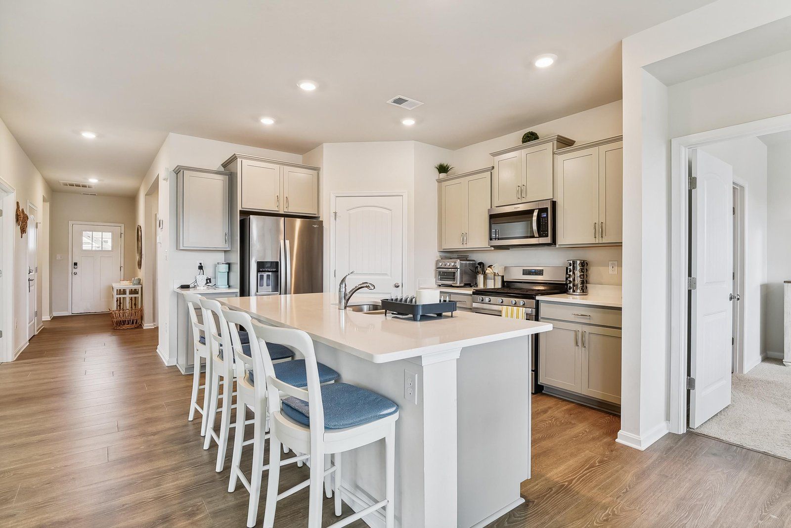 A modern kitchen with a central island, bar stools, stainless steel appliances, and light-colored cabinetry.