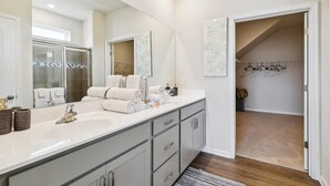 Un baño moderno con un espejo grande, dos lavamanos y un vestidor con zapatero.