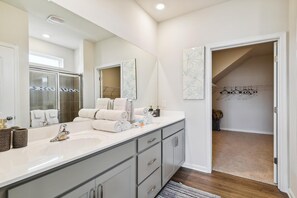 Un baño moderno con un espejo grande, dos lavamanos y un vestidor con zapatero.