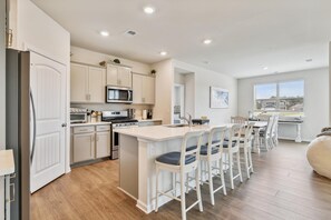 Una cocina moderna con armarios blancos, una isla central con taburetes altos y un comedor con vista a la playa.