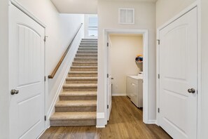 Un pasillo con una escalera con alfombra, puertas blancas y un área de lavandería con lavadora.