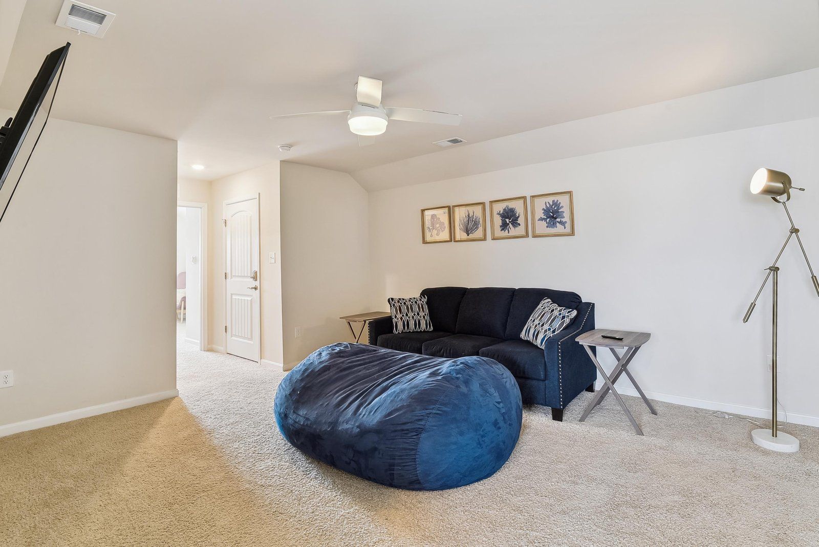 Une pièce avec un canapé bleu foncé, une petite table, un lampadaire et un ventilateur de plafond.