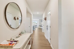 A hallway with a white door, a mirror, and a bench with a tray of items. - Beach Club Getaway! Ample Amenities and Short Drive to Beaches! (OceanView)
