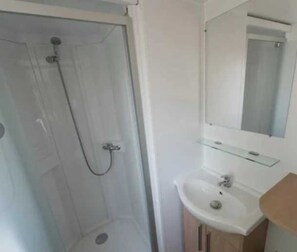 Bathroom features a glass-enclosed shower, sink with mirror, and wooden cabinet.