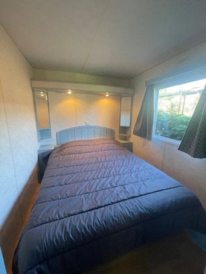 Een klein bed met hoofdeinde, een raam met gordijnen en een spiegel aan de muur.