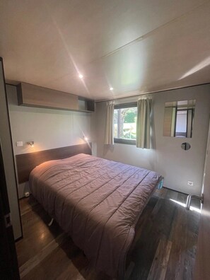 Quarto com uma cama, janela com cortinas, espelho e porta.