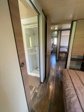 A modern interior with a glass-enclosed shower, a bed, and a compact kitchenette.