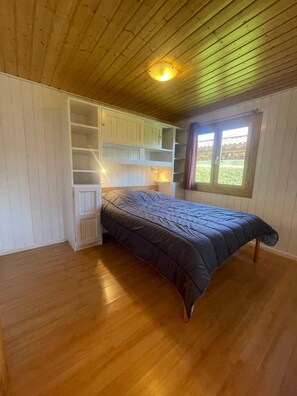 A bedroom with a bed, built-in shelving, a window, and a ceiling light.