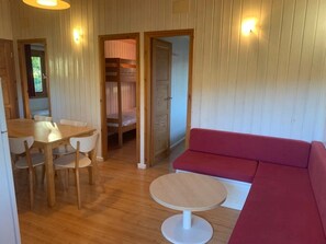 A room with a wooden floor, a round table, a red sofa, and a wooden door leading to another room.