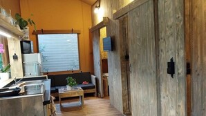 Une pièce chaleureuse avec un décor intérieur en bois, un canapé, une table à manger agrémentée d’un panier de fruits et un téléviseur fixé au mur.
