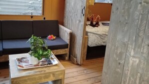 Une pièce chaleureuse avec un plancher en bois, un canapé, une petite table sur laquelle est posée une plante, et un téléviseur fixé au mur.