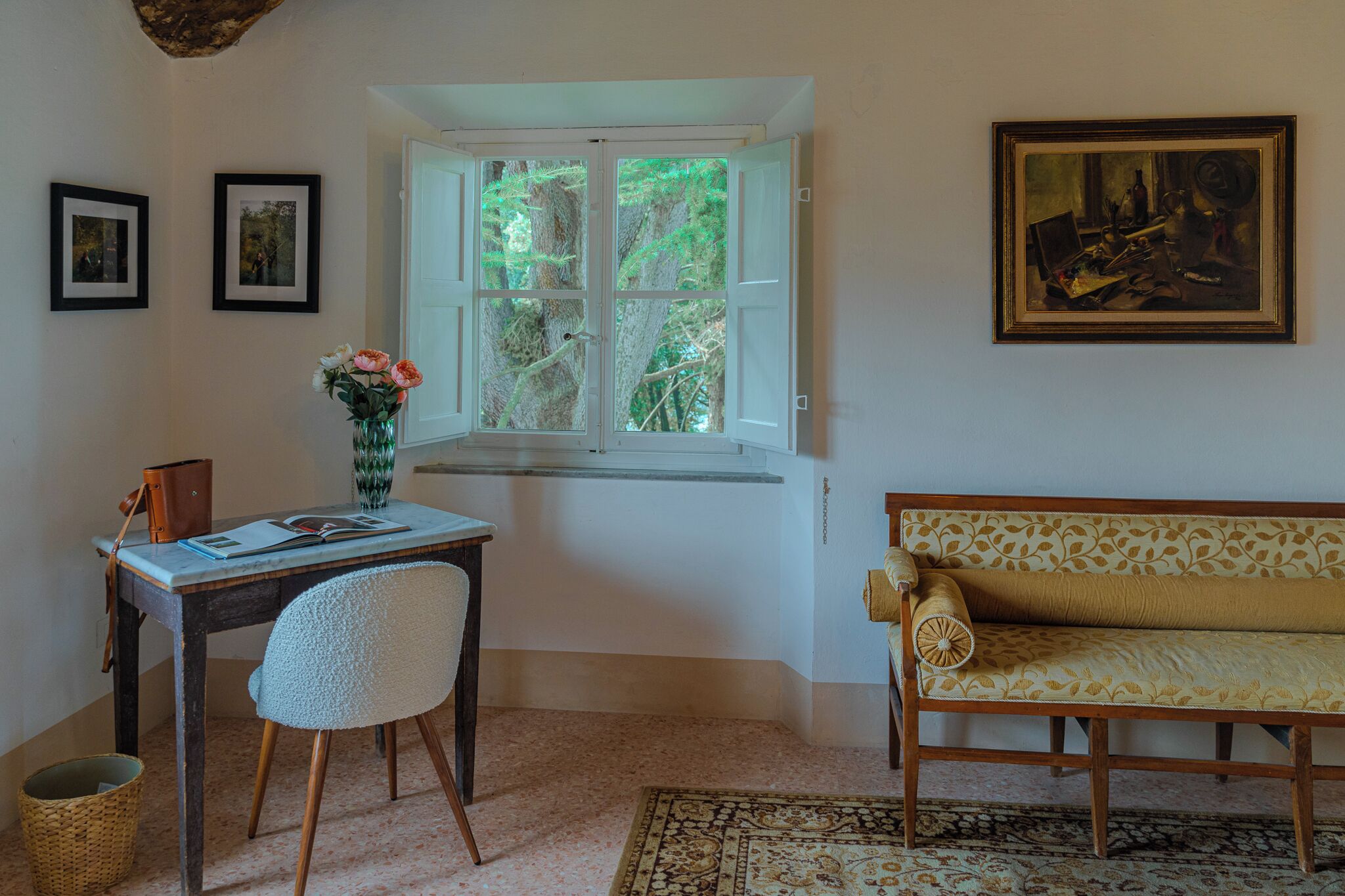 A room with a desk, chair, window, sofa, and artwork.