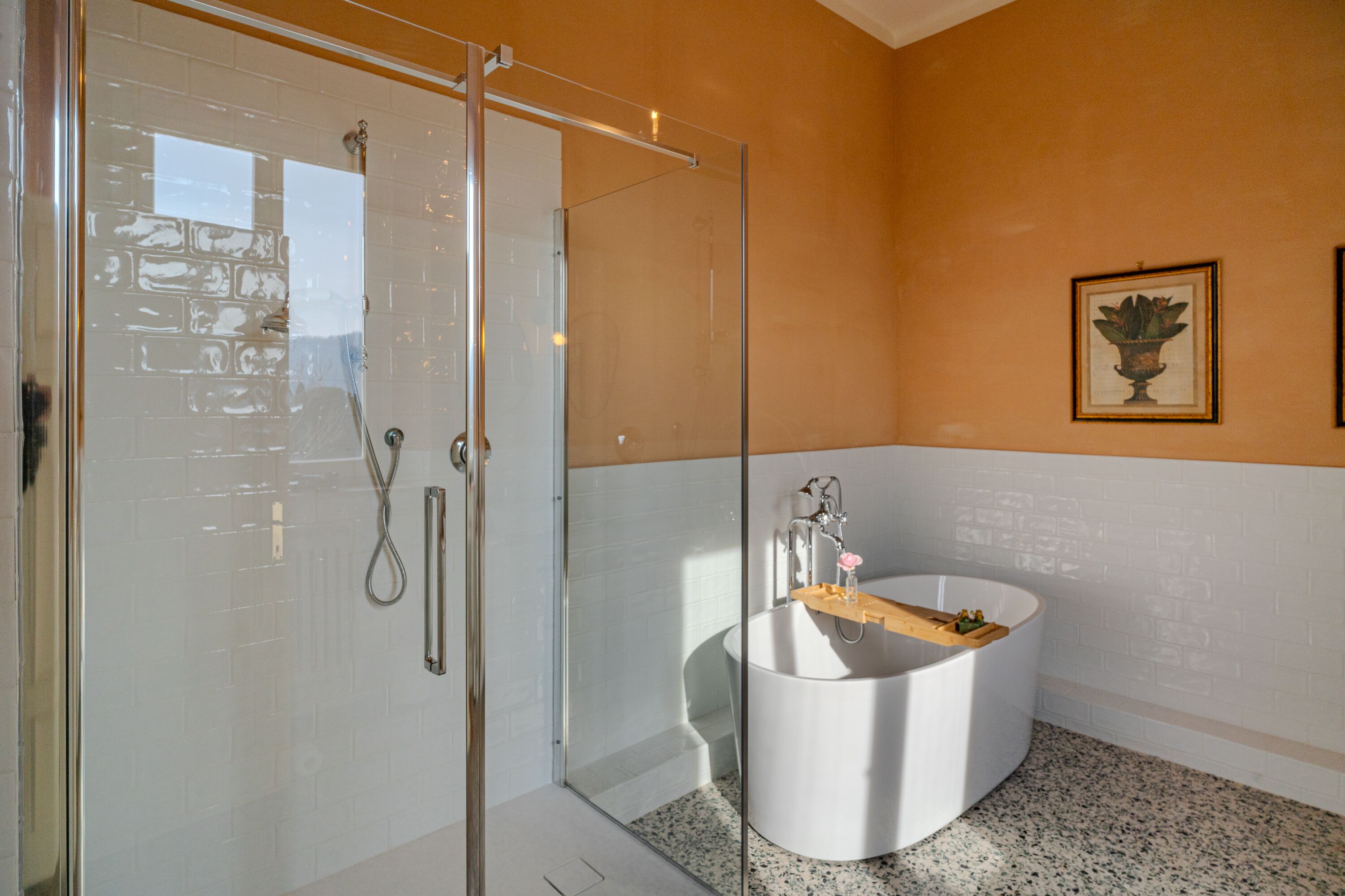 Ein modernes Badezimmer mit Duschkabine aus Glas, einer freistehenden Badewanne und einem gerahmten Kunstwerk an der Wand.
