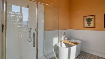 Ein modernes Badezimmer mit Duschkabine aus Glas, einer freistehenden Badewanne und einem gerahmten Kunstwerk an der Wand.