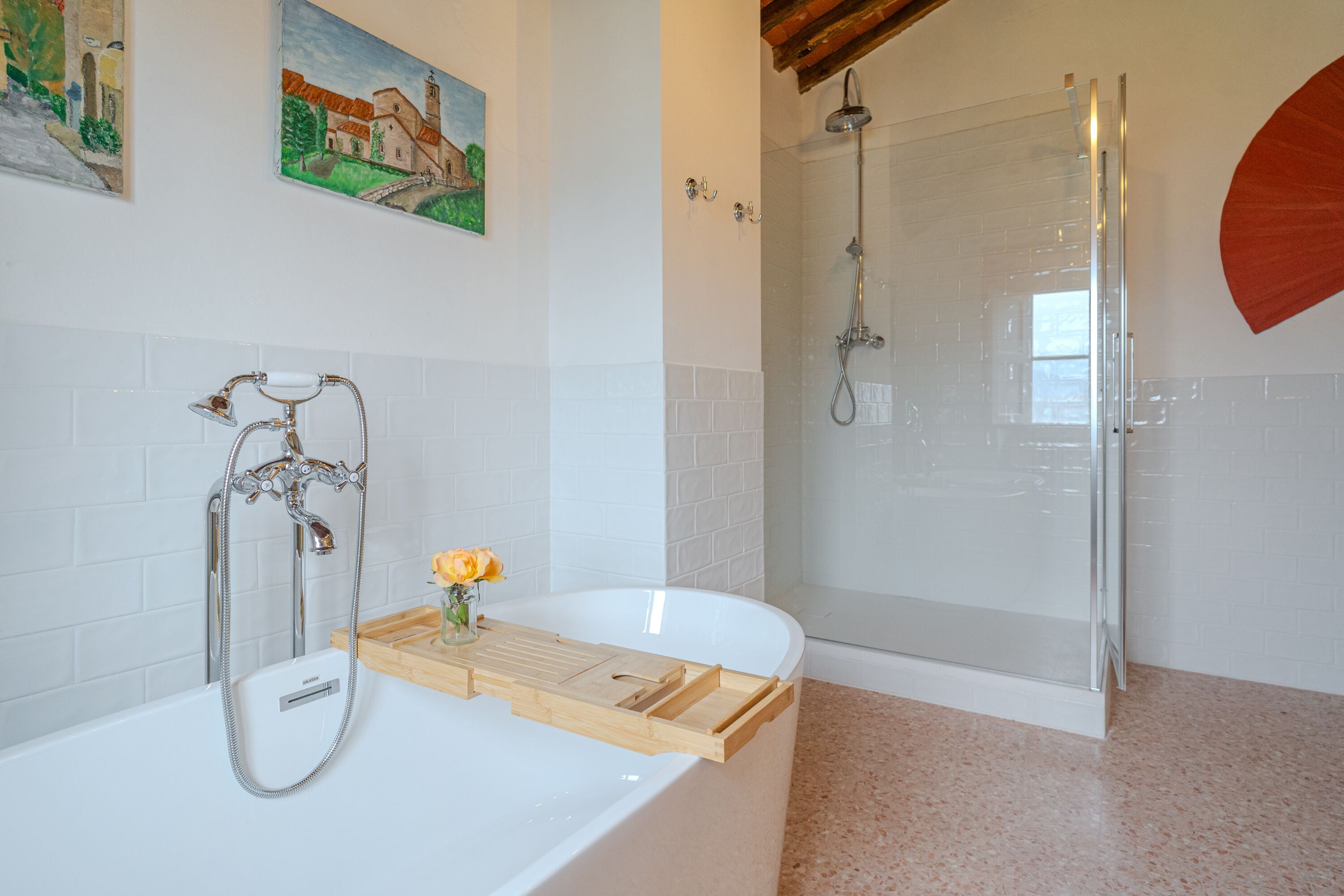 Un baño moderno con una bañera blanca, una ducha con cerramiento de vidrio y una bandeja de madera con un jarrón de flores.