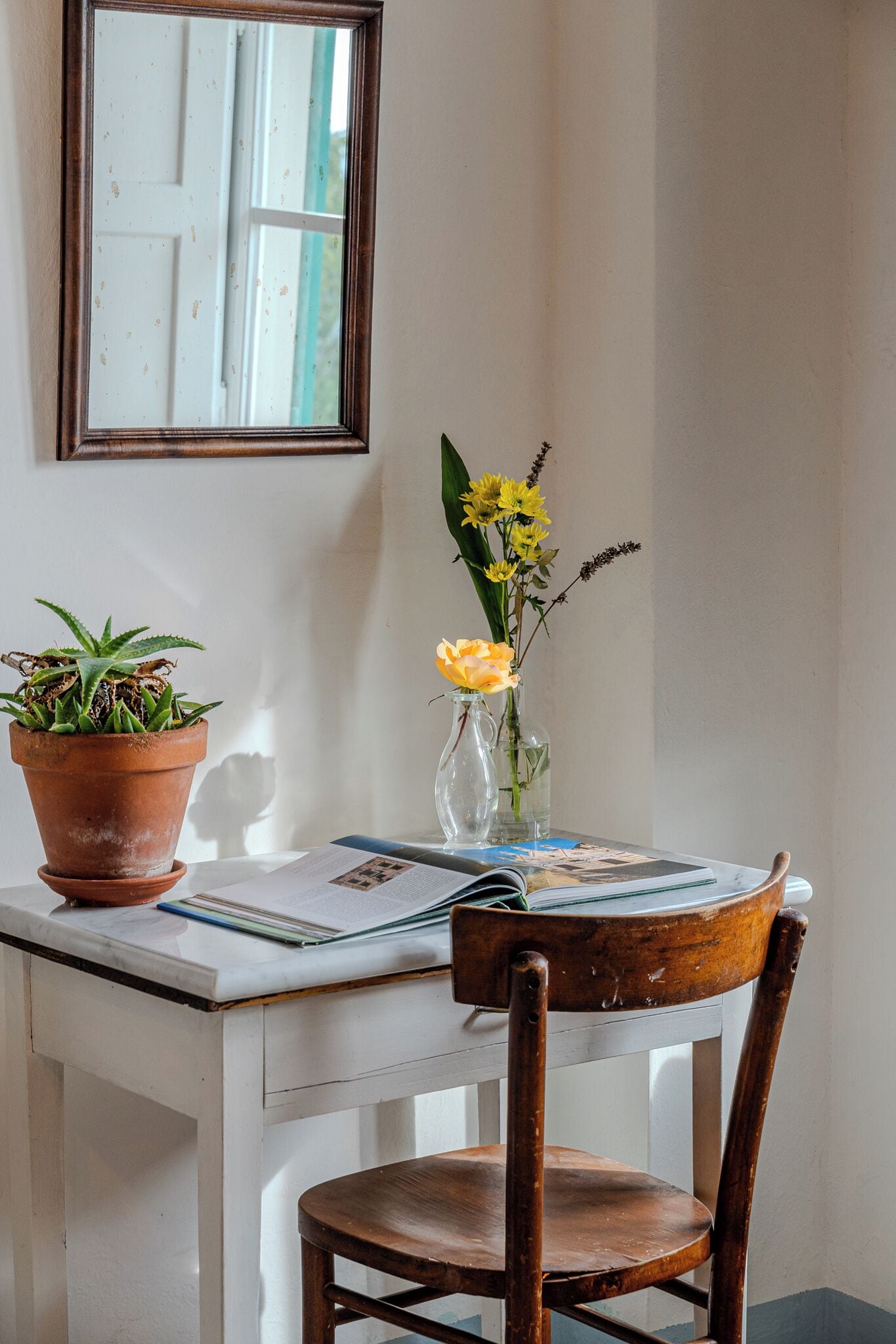 A wooden chair and desk with a potted plant and a vase with yellow flowers.
